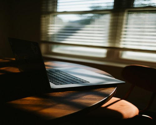 A person working on a laptop near a large window with soft natural lighting, illustrating high visual comfort in a home office setup.